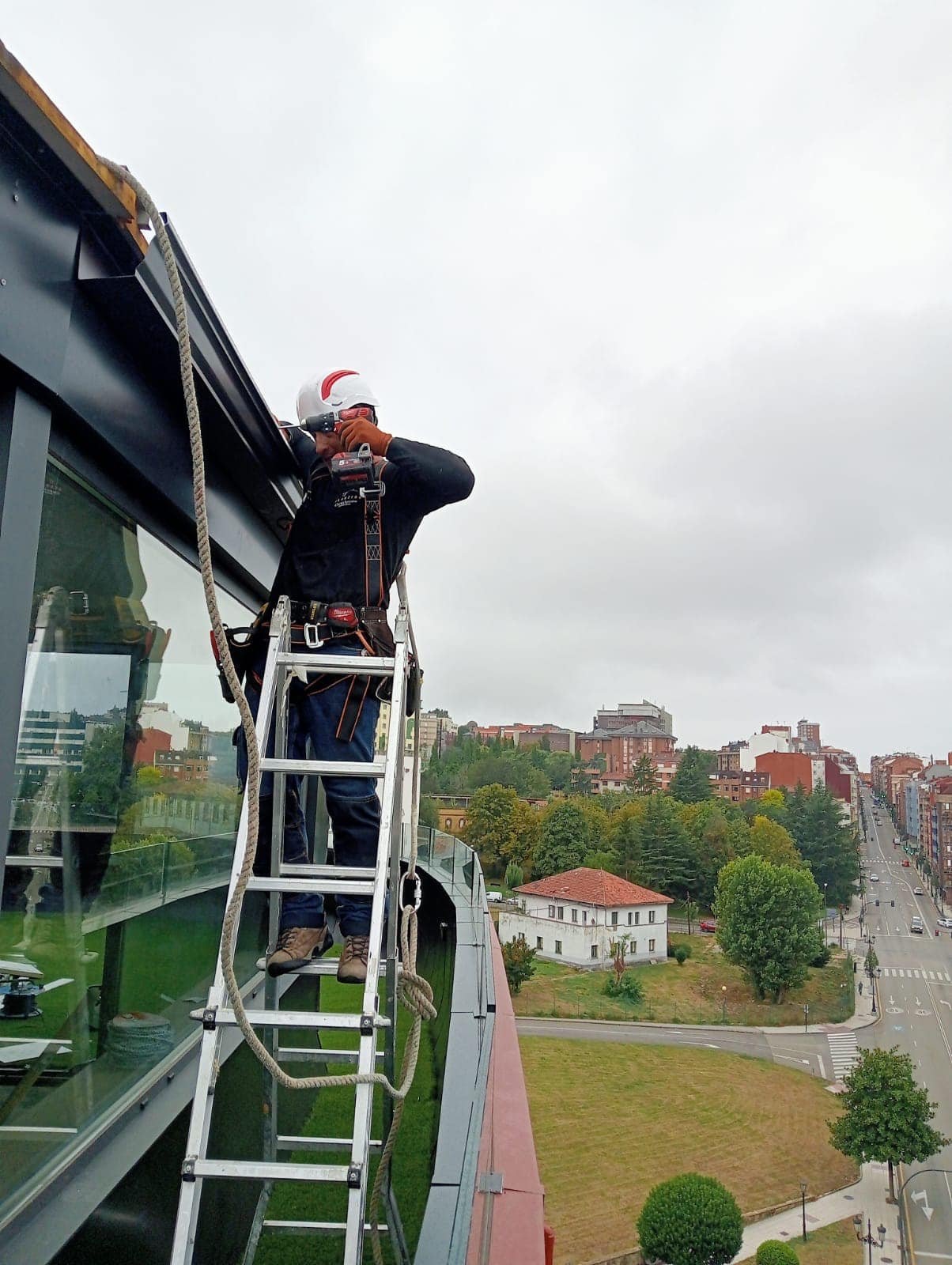 Instalador en escalera sobre la cubierta de un ático fijando un canalón negro